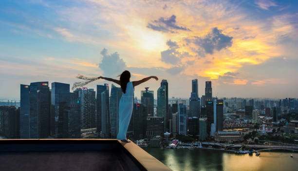 Young woman standing hands rised on the rooftop of skyscraper in Singapore city